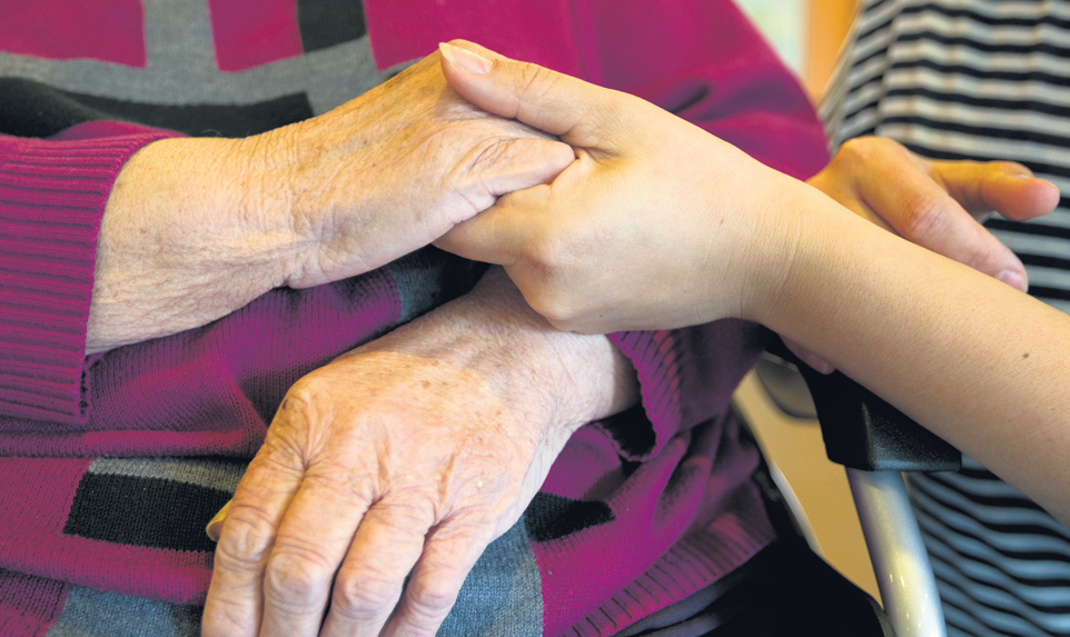 Zorgmedewerker houdt hand van oudere persoon vast