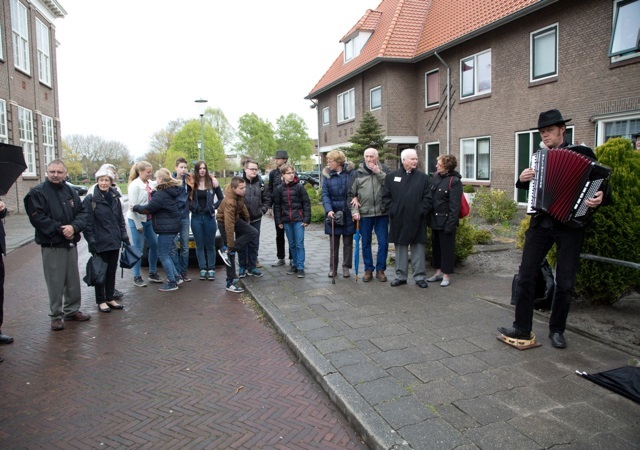 Publiek bij de onthulling van herdenkingsstenen luisterend naar live muziek